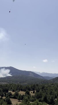 Breathtaking aerial footage of a firefighting helicopter dropping water on a massive pine forest wildfire during a hot summer afternoon