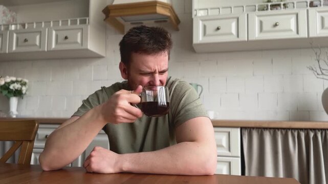 man drinking coffee and suffer kitchen setting with wooden table and ceramic pitcher, daily life scene with green shirt and brown wooden table, close-up view of man enjoying coffee in home.
