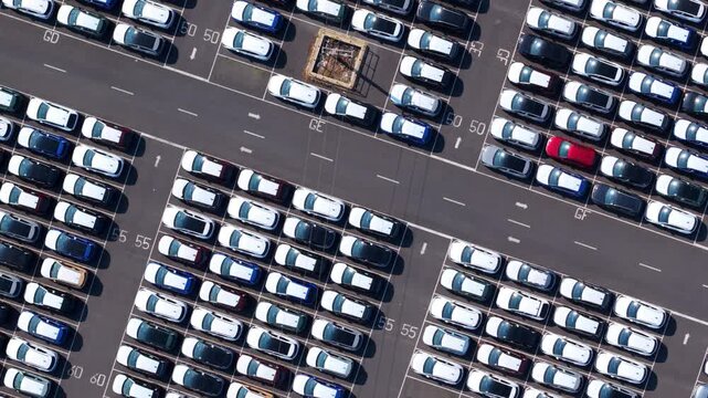 Aerial view looking directly down at a sprawling vehicle import hub featuring uniform rows of thousands of newly manufactured cars.