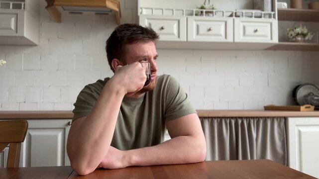 man drinking coffee and suffer kitchen setting with wooden table and ceramic pitcher, daily life scene with green shirt and brown wooden table, close-up view of man enjoying coffee in home.