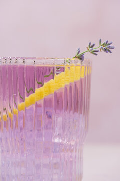 Close up refreshing lavender lemonade served in elegant ribbed glasses with fresh lavender sprigs, ice cubes and a lemon twist. Light purple citrus drink on a soft pastel background