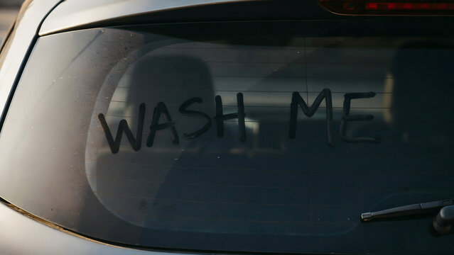 The phrase wash me written in the dust on a dirty rear car window