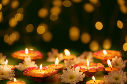Lit clay diyas and white flowers with golden bokeh lights for Diwali