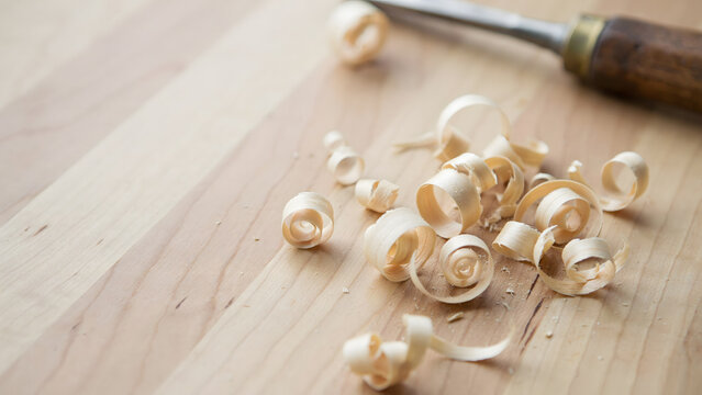 Wood shavings and a metal chisel on a clean light brown wooden workbench