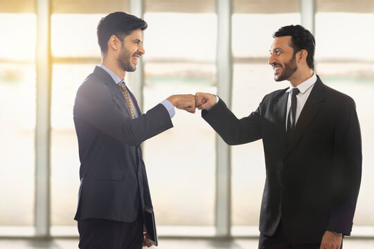 Corporate employees in formal business suit standing While making fist bump looking at each other,smiling.