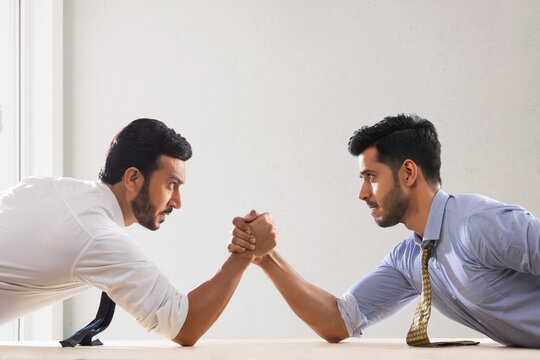 Corporate employees in formal clothing engaged in an arm wrestling match.