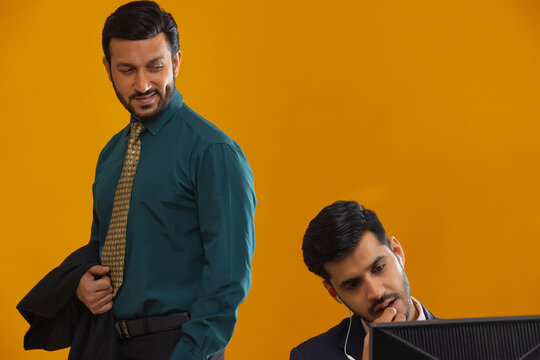 A corporate employee in formal clothing smirking while looking at colleague who is working on laptop.