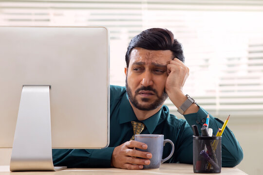 A corporate employee in formal clothing looking disinterestedly at desktop screen with drowsy eyes in office.