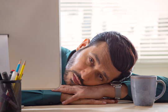 A corporate employee in formal clothing looking at desktop screen with drowsy eyes in office.