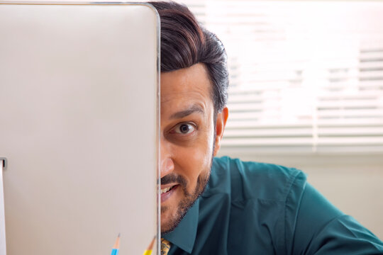 A corporate employee's face partially visible peeping out from the desktop screen in office.