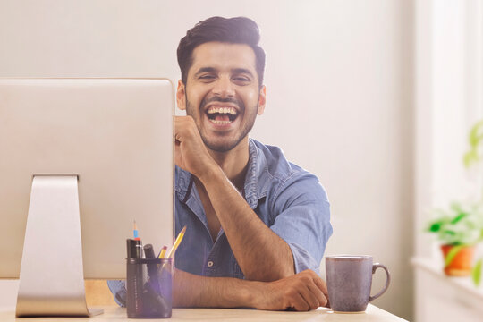 A corporate employee in formal clothing smiling behind his desktop at workdesk.