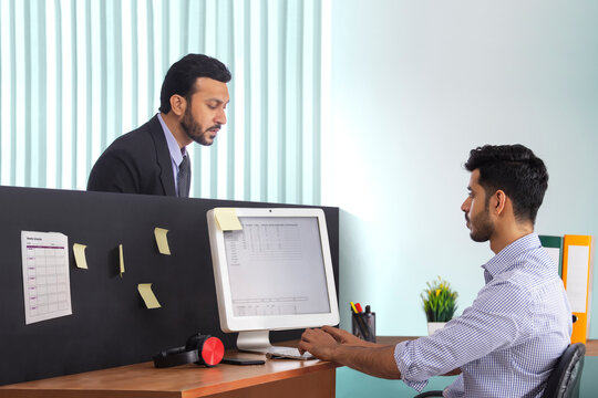 A boss in formal business suit surveying the work of subordinate employee at workdesk.