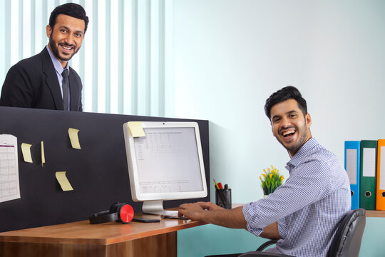 Corporate employees together at workdesk with one working on computer and the other standing.
