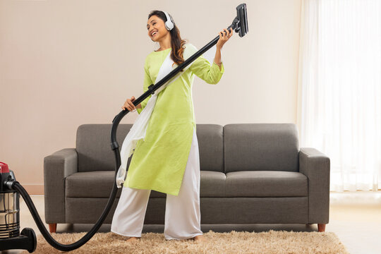 Young woman listening music and having fun with vacuum cleaner