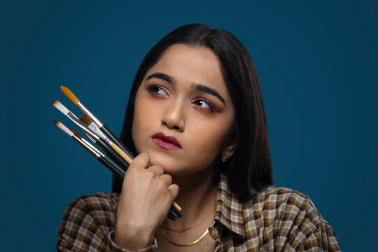 Young artist girl holding brushes and thinking for a new idea