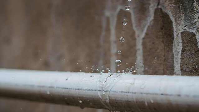 Water leaking from a damaged white plastic pipe against a concrete wall