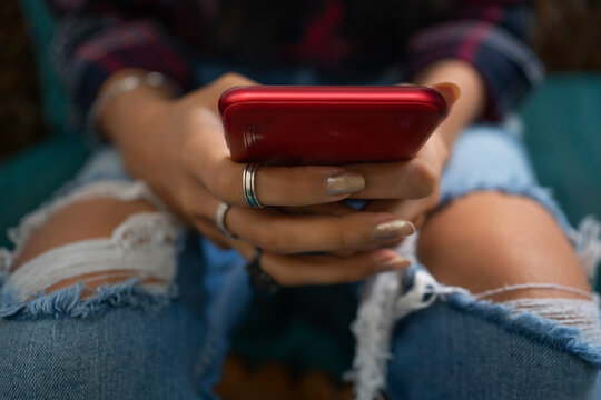 The hands of a young woman wearing ripped jeans holding a mobile phone.
