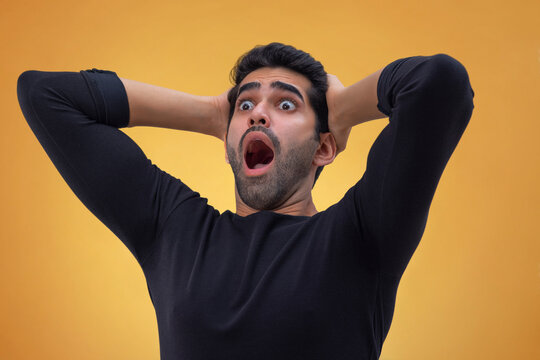Portrait of a stunned young man with wide eyes,hands on his head and looking elsewhere with open mouth