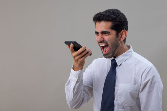 An angry young man in a white shirt shouting while talking on Smartphone