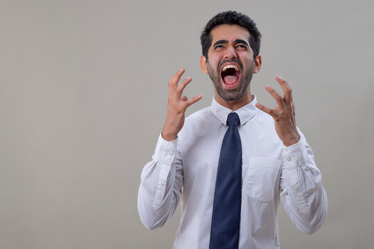 Portrait of an angry young man in white shirt shouting with raising his hands