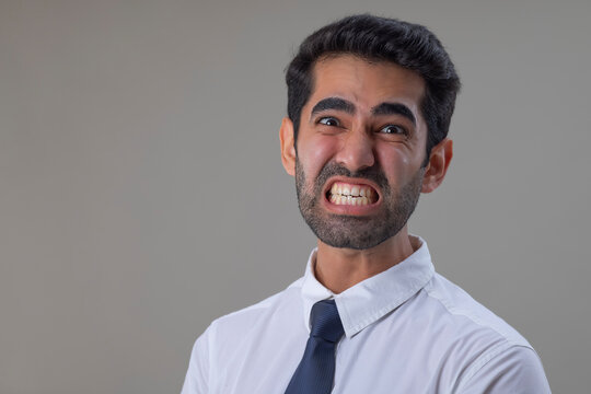 Portrait of an angry young man in white shirt looking at the camera with teeth clenching