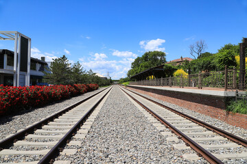 Obraz premium Vintage Train Station Platform and Railway Tracks Under Clear Blue Sky