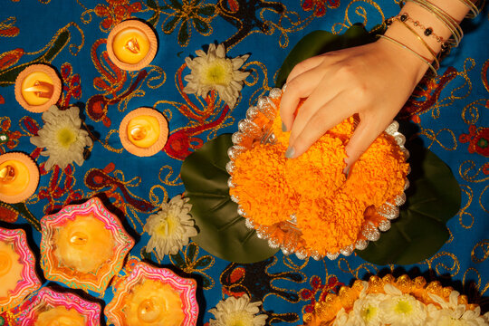 Cropped hand arranging marigold flowers with lit diyas for Diwali celebration