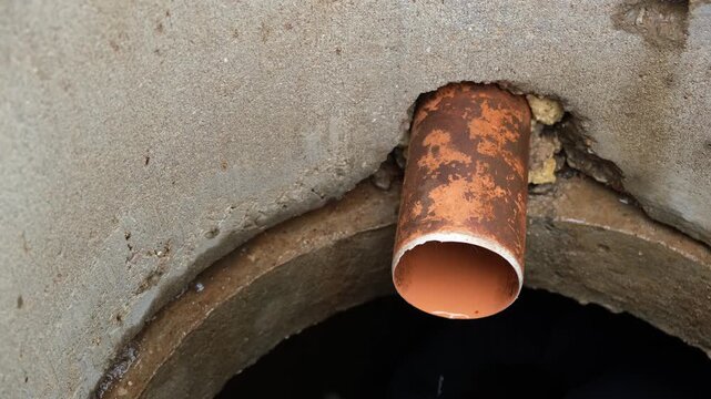 An orange plastic pipe protrudes from a concrete ring into overflow sewer well. Drainage system. A service cleaning of blocked sewer. Maintenance work, utility service, underground infrastructure. 4k.