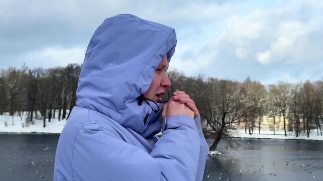 Woman in bright blue hooded parka standing beside snowy lake with bare trees, cloudy winter sky, soft diffuse light, quiet cold landscape and reflective water, with woman, winter, snowy detail