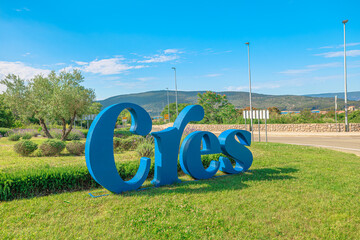 Large blue Cres sign stands on a grassy area, a landmark welcoming visitors to the Croatian island with surrounding green hills and a bright summer sky of Cres Island in Croatia © bennymarty