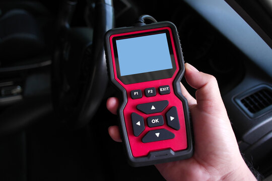 A hand holding a OBD2 code reader with blank screen inside a car cabin, ready to diagnose vehicle errors, check engine issues, and perform auto maintenance