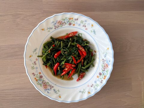 Stir-fried morning glory or Pak Boong Fai Daeng on a rustic wooden table.