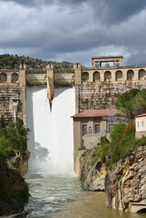 Naklejka premium The water cycle: the Oliana dam in Catalonia is releasing water, whilst dark nimbostratus clouds herald a storm that will continue to fill reservoir.