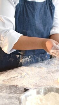 Vertical video: Dusting flour, cook in apron kneading dough for baking at counter with metal bowl