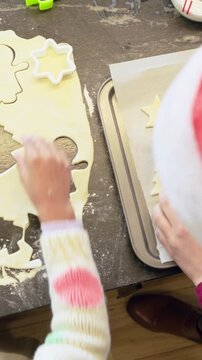 Vertical video: Cutting dough, red mom using molds while kid placing holiday shapes on tray to bake