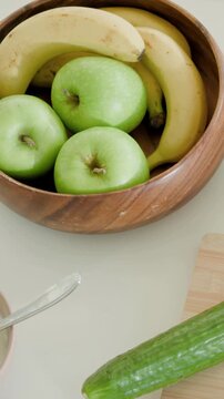 Vertical video: Panning camera over bowl with apples, bananas on counter for prep, cucumber, peeler