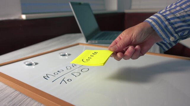 Worker puts coffee reminder note on Monday morning schedule whiteboard
