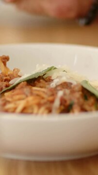 Vertical video: Hand entering twirling fork in bowl on wood table, lifting noodles toward mouth
