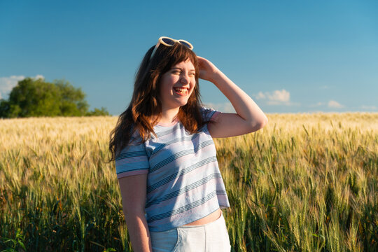 Happy young woman smiling in wheat field during summer sunset