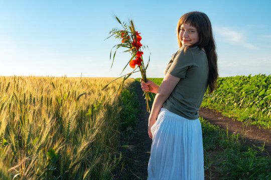Young woman holding bouquet of red poppies in wheat field at sunset