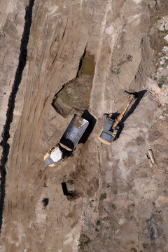 Excavator and dump truck performing earthmoving work at construction site aerial view