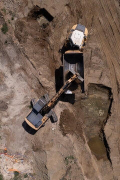 Excavator and dump truck performing earthmoving work at construction site aerial view