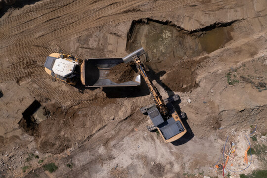 Excavator and dump truck performing earthmoving work at construction site aerial view