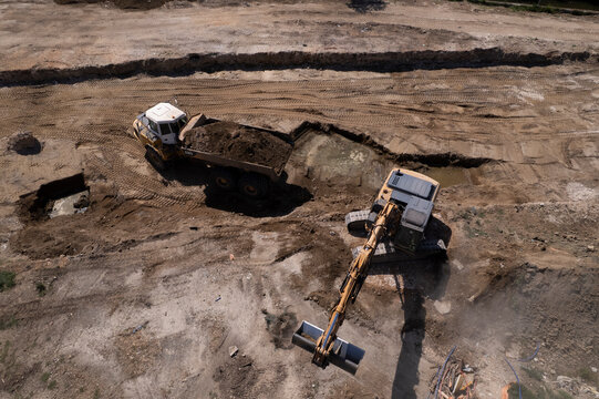 Excavator and dump truck performing earthmoving work at construction site aerial view
