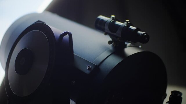 Close up view of a small finderscope mounted on the main optical tube of a large professional astronomical telescope inside a dark observatory