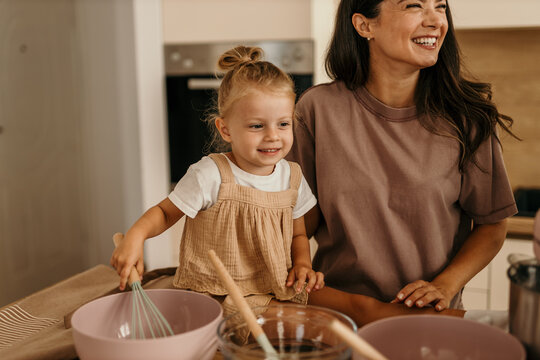 Mother and daughter smiling while baking together in kitchen