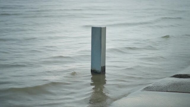 Slow motion B-roll of a flood water level marker submerged in coastal seawater. Perfect for climate crisis news, insurance risk analysis, government reports, and corporate landing pages.