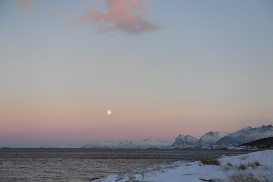 Landscape shot highlighting a near full moon over the rugged mountains of arctic Norway, near Bodo, during golden hour.