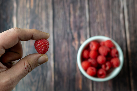 Fresh Raspberry Held in Hand with Bowl