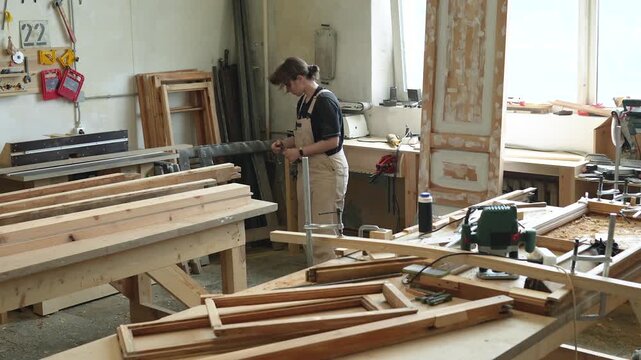 Concentrated professional woman crafter engaged in creative process of restoration in workshop, skilled female master working with wooden details and clamps tool on worktable, fixing parts to surface.